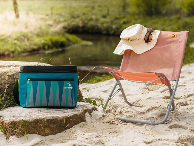 Laad afbeelding in galerijtoner, Groene koeltas naast roze campingstoel op zand.