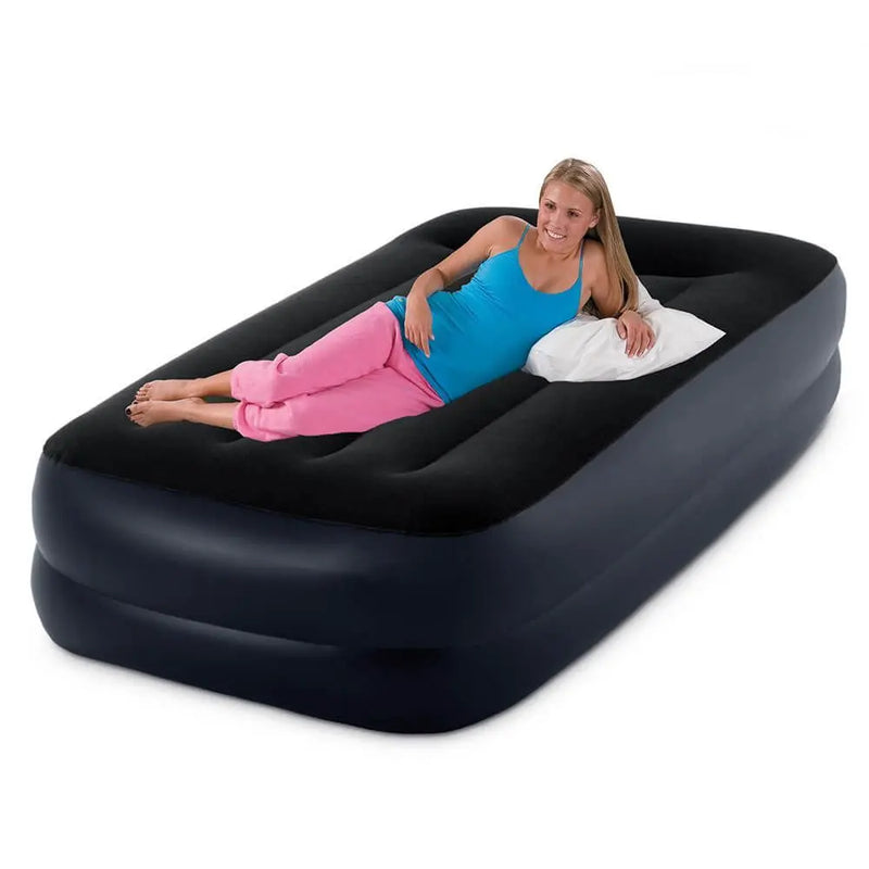 Laad afbeelding in galerijtoner, Vrouw in blauwe top en roze broek ligt op een Intex Pillow Rest Raised Eenpersoons Luchtbed van Intex met wit kussen, glimlachend-ideaal voor comfortabel slapen. Gebruik een elektrische pomp voor snel en makkelijk oppompen.