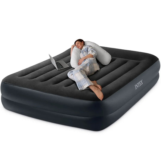 Een vrouw in pyjama ontspant met haar laptop en kussen op een Intex Pillow Rest Raised Tweepersoons Luchtbed en geniet van het comfort van de Intex Fiber-Tech® binnenstructuur.