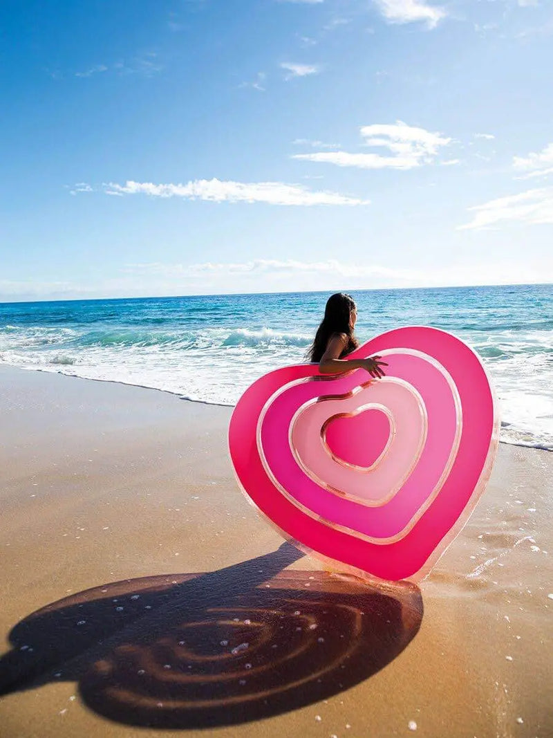 Laad afbeelding in galerijtoner, Vrouw aan zee met een hartvormig luchtbed in haar hand.