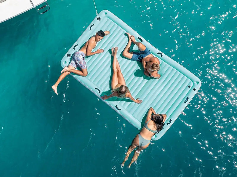 Laad afbeelding in galerijtoner, Vier personen ontspannen zich op de Intex Waterlounge van Intex, drijvend in helderblauw water en genietend van een zonnige dag.