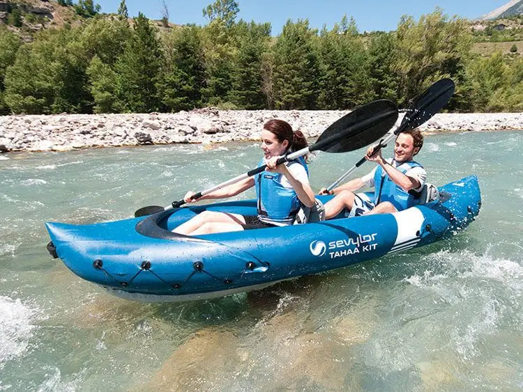 Laad afbeelding in galerijtoner, Twee personen peddelen in een Sevylor Tahaa Opblaaskayak van Sevylor, gemaakt van UV-bestendig PVC, over een heldere, ondiepe rivier omgeven door bomen.