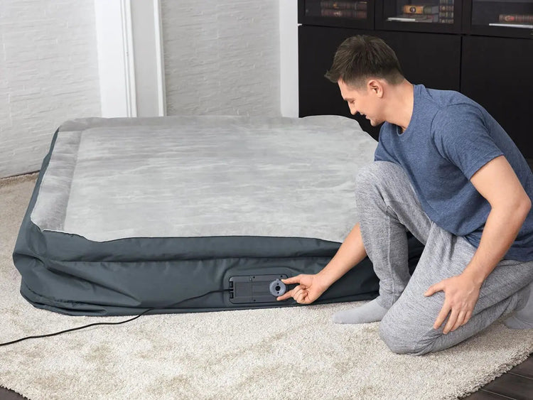 Man pompt een grijs opblaasbaar luchtbed op met behulp van een ingebouwde pomp