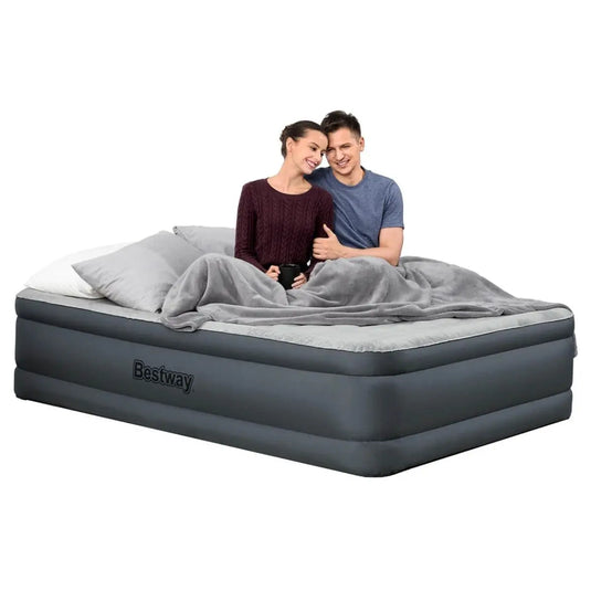 Een lachend stel ontspant op het Bestway Tweepersoons Luchtbed Tough Guard Comfy en geniet van de Snugable Top, met kussens en een grijze deken voor extra comfort.