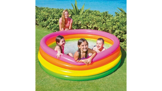 Drie kinderen zwemmen in een rond opblaasbaar kinderzwembad Intex Sunset Glow met een groene, gele, oranje en roze band terwijl het bad in de achtertuin staat
