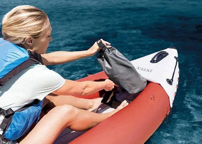 Laad afbeelding in galerijtoner, Een persoon in een reddingsvest plaatst een grijze droogzak op een Intex Excursion Pro K1 opblaasbare kajak
