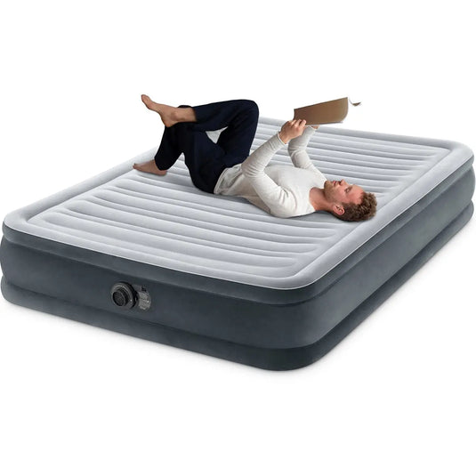 Een man ontspant met opgetrokken benen en leest een boek op het Intex Comfort Pluche Luchtbed Twijfelaar met Fiber-Tech® technologie tegen een witte achtergrond.