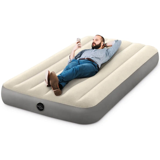 Een man ligt comfortabel op het Intex Deluxe Eenpersoons Luchtbed terwijl hij naar zijn telefoon kijkt.