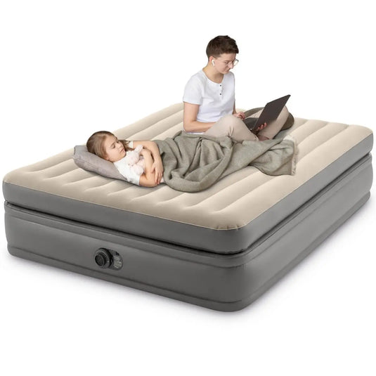 Een volwassene gebruikt een laptop terwijl een kind slaapt op het Intex Prime Comfort Tweepersoons Luchtbed met Fiber-Tech technologie, deken, kussen en een geïntegreerde elektrische pomp voor snel oppompen.