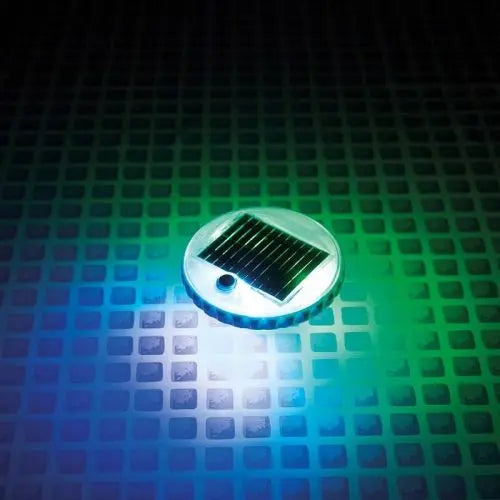 De Intex Solar Drijflicht van Intex gloeit met blauw en groen licht op een oppervlak met rasterpatroon, waardoor hij perfect is als jacuzzi-lamp.