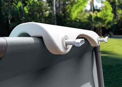 De Intex Zwembadstoel, een witte, gebogen zwembadhaak van Intex, wordt bevestigd aan de zijkant van een zwembad met frame in de tuin, met groen gras en bomen op de achtergrond.