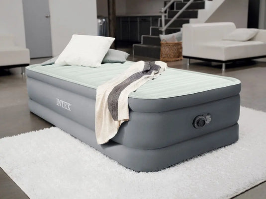 Intex PremAire I Eenpersoons Luchtbed met een ingebouwde pomp staat opgeblazen in de woonkamer met twee kussens en een dekentje