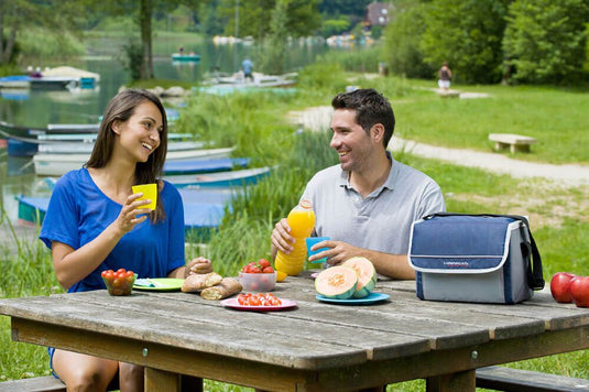 Twee mensen drinken aan een picknicktafel met naast hun een blauwe koeltas.